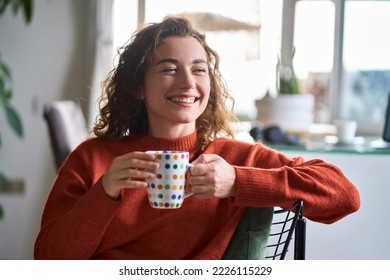 Young smiling pretty woman holding cup drinking warm tea or coffee relaxing dreaming at home. Happy positive lady enjoying hot drink daydreaming with mug in hands in cold cozy winter weekend morning. - Powered by Shutterstock