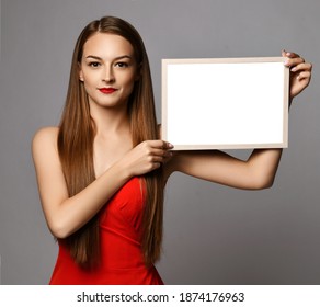 Young smiling pretty woman in red dress with long silky straight hair holding white black for text and lettering mockup in hands over grey background. Haircare, beauty, wellness, hairstyle concept