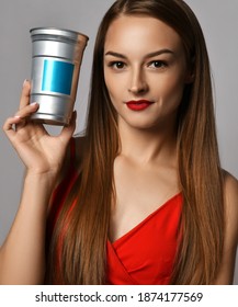 Young smiling pretty woman in red dress standing with long silky straight hair holding treatment care cosmetics for hair in hands over grey background. Haircare, beauty, wellness, hairstyle concept