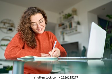 Young smiling pretty woman student using laptop elearning or remote working at home office using laptop computer watching webinar, learning web course, studying online sitting at table, writing notes. - Shutterstock ID 2226115277