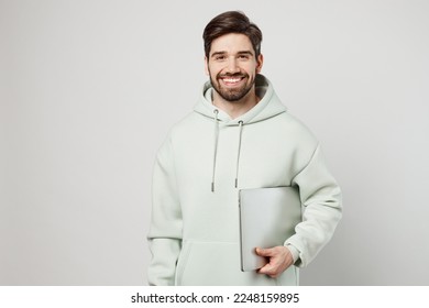 Young smiling programmer happy fun caucasian man wearing mint hoody hold use work on laptop pc computer look camera isolated on plain solid white background studio portrait. People lifestyle concept - Shutterstock ID 2248159895