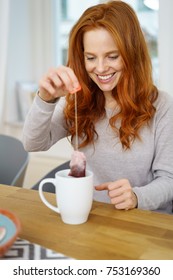 Young Smiling Red-haired Woman Removing Tea Bag From Mug