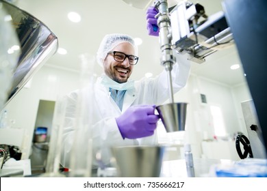Young smiling researcher with gloves and hair protection working on the lab machine.