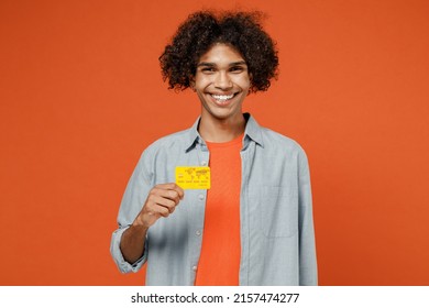 Young Smiling Rich Happy Student Black Man 50s Wearing Blue Shirt T-shirt Look Camera Hold In Hand Credit Bank Card Isolated On Plain Orange Color Background Studio Portrait. People Lifestyle Concept