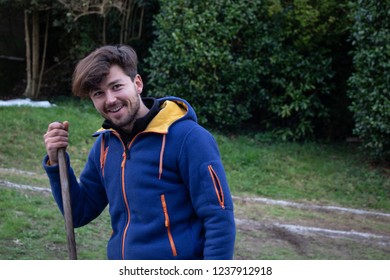 Young smiling in a rural setting, holding a wooden stick with vegetation on the back - Powered by Shutterstock