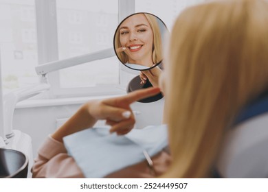 Young smiling satisfied fun happy calm woman 20s reflected in mirror sitting at dental office chair indoor light cabinet look at teeth toothy smile whitening result Healthcare caries enamel treatment. - Powered by Shutterstock