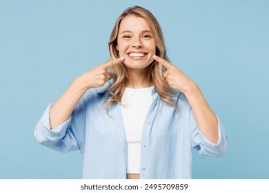 Young smiling satisfied happy woman she wearing white top shirt casual clothes point index fingers on opened mouth teeth isolated on plain pastel light blue cyan background studio. Lifestyle concept