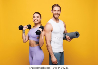 Young smiling strong fitness trainer instructor sporty two man woman wearing blue clothes spend time in home gym hold yoga mat dumbbells isolated on plain yellow background. Workout sport fit concept - Powered by Shutterstock