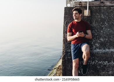 Young smiling strong sporty toned fit sportsman man in sports clothes use mobile cell phone listen music earphones warm up train at sunrise sun dawn over sea beach outdoor on pier seaside in morning - Powered by Shutterstock