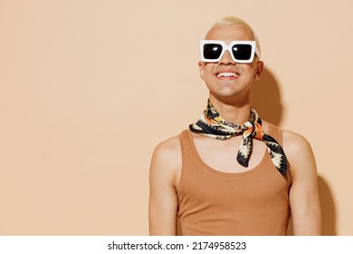 Young smiling stunning fashionable stylish blond latin gay man in beige tank shirt neck scarf sunglasses isolated on plain light ocher color background studio portrait. People lgbt lifestyle concept. - Powered by Shutterstock