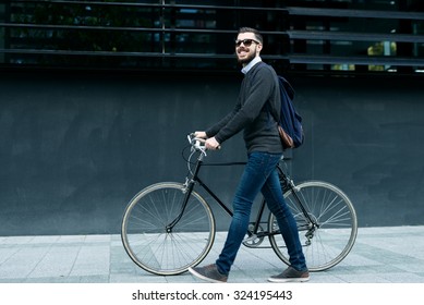 A young smiling stylish businessman pushing a bicycle while going to work.