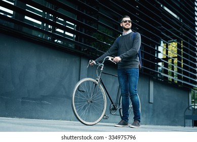 A young smiling stylish businessman pushing a bicycle while going to work. - Shutterstock ID 334975796