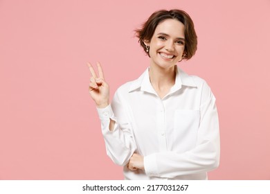 Young smiling successful employee business woman corporate lawyer 20s in classic formal white shirt work in office show victory v-sign gesture isolated on pastel pink color background studio portrait