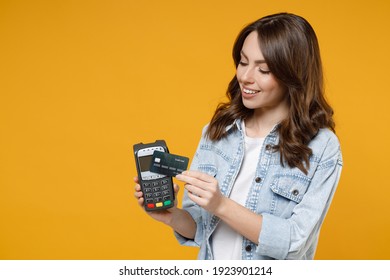 Young smiling successful woman 20s in denim shirt white t-shirt hold wireless modern bank payment terminal to process and acquire credit card payments isolated on yellow background studio portrait. - Shutterstock ID 1923901214