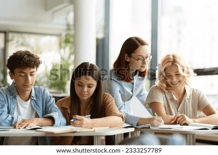 Young smiling teacher or tutor having lesson, assisting, explaining something, studying, learning language with school children sitting in classroom. Education concept 