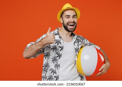 Young smiling tourist man in beach shirt hat hold inflatable ball travel abroad on weekends show thumb up isolated on plain orange background studio portrait. Summer vacation sea rest sun tan concept