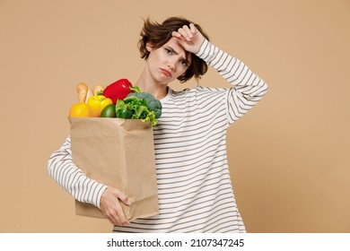 Young Smiling Vegetarian Woman 20s In Casual Clothes Hold Paper Bag With Vegetables After Shopping In Greengrocery Put Hand On Forehead Have Headache Isolated On Plain Pastel Beige Background Studio