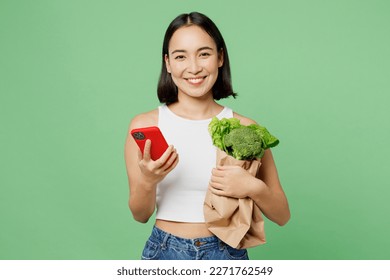 Young smiling vegetarian woman wear white clothes hold broccoli use mobile cell phone browsing internet isolated on plain green background Proper nutrition healthy fast food unhealthy choice concept - Powered by Shutterstock