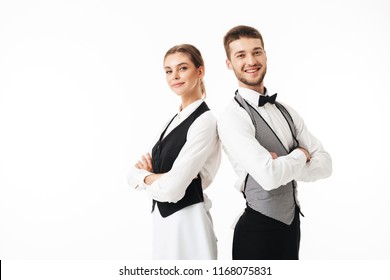 Young smiling waiter and beautiful waitress in white shirts and vests sstanding back to back happily looking in camera with arms folded over white background - Powered by Shutterstock