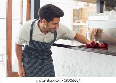 Young Smiling Waiter Cleaning Countertop With Sponge