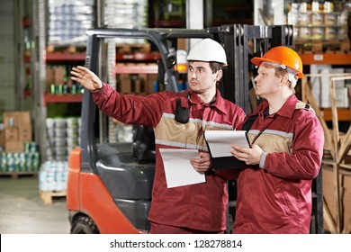 Young Smiling Warehouse Workers In Uniform In Front Of Forklift Stacker Loader