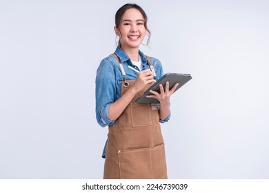 young smiling welcome asian female woman business owner wear apron hand holding tablet ready for your order or manage food inventory stock for her coffee shop restaurant studio shot white background - Shutterstock ID 2246739039