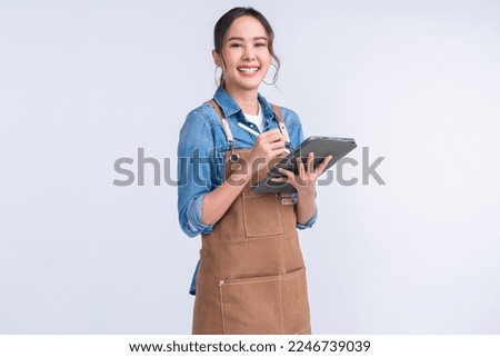 young smiling welcome asian female woman business owner wear apron hand holding tablet ready for your order or manage food inventory stock for her coffee shop restaurant studio shot white background