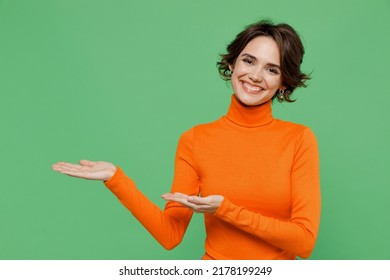 Young Smiling Woman 20s Wear Casual Orange Turtleneck Point Hands Arms Aside On Workspace Area Mock Up Isolated On Plain Pastel Light Green Color Background Studio Portrait. People Lifestyle Concept