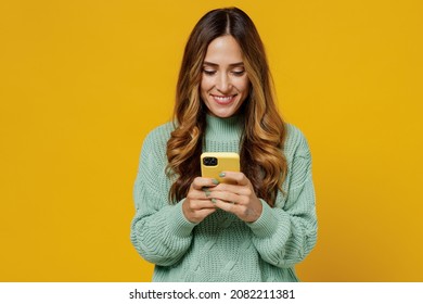 Young smiling woman 30s wearing green knitted sweater hold in hand use mobile cell phone chatting browsing internet isolated on plain yellow color background studio portrait. People lifestyle concept - Shutterstock ID 2082211381