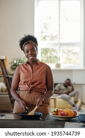 Young Smiling Woman Of African Ethnicity Looking At You While Standing By Electric Stove