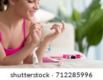 Young smiling woman applying lacquer polish, painting fingernails with colorless protective enamel, doing french homemade manicure at home with tools set, perfect healthy nails care, close up view