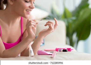 Young smiling woman applying lacquer polish, painting fingernails with colorless protective enamel, doing french homemade manicure at home with tools set, perfect healthy nails care, close up view