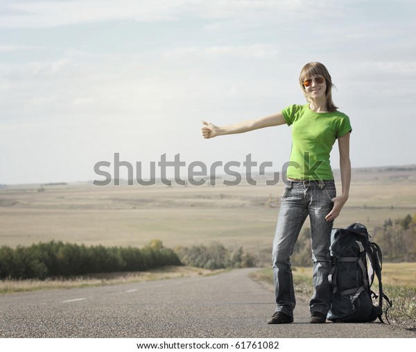 Young smiling woman with backpack catching a car on\
empty road