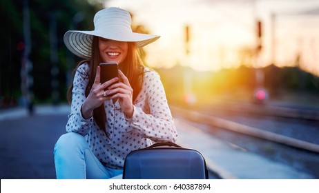 Young Smiling Woman With Baggage On Train Station Using Smart Phone