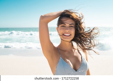 Young smiling woman in bikini at tropical beach looking at camera. Portrait of beautiful latin girl in swimwear with ocean in background. Happy tanned hispanic woman relaxing at sea and copy space. - Powered by Shutterstock