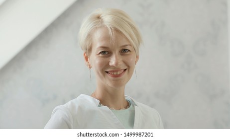 Young smiling woman - blond beautician in white lab coat.