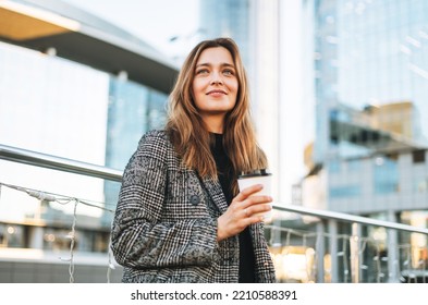 Young smiling woman in coat with paper coffee cup in evening city street - Powered by Shutterstock