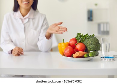Young smiling woman doctor pointing and recommending fresh vegetables for dieting and losing weight during online consultation, cropped composition. Healthy lifestyle concept - Shutterstock ID 1836969082