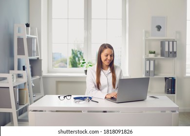 Young Smiling Woman Doctor Therapist Sitting In Medical Clinic Office With Laptop And Communicating Online With Somebody. Distant Working, Telemedicine Concept