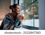 Young smiling woman drinking tea and looking through the window at home. Copy space.