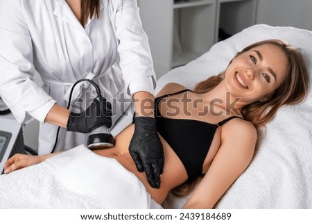 Young smiling woman during ultrasound cavitation body contouring treatment procedure at beauty salon 