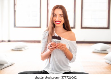 Young And Smiling Woman Eating Black Chocolate Without Worrying About Calories And Weight Sitting In The Gym