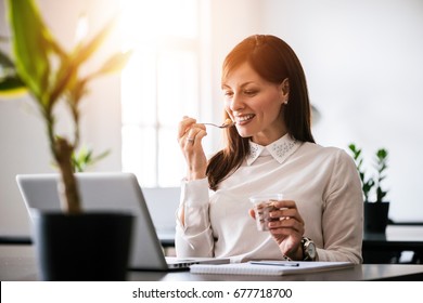 Young Smiling Woman Eating Ice Cream In Office