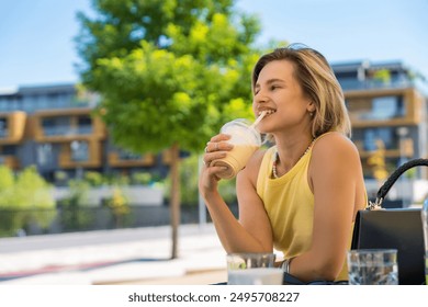 Young smiling woman enjoying a refreshing iced coffee in plastic cup at an outdoor cafe in summer - Powered by Shutterstock