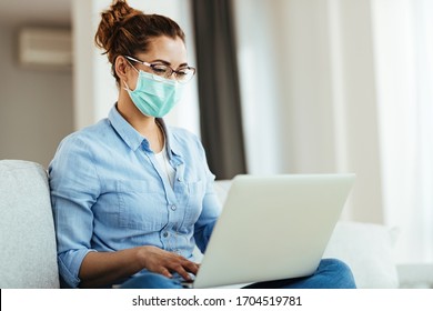 Young Smiling Woman With Face Mask Using Computer While Relaxing In The Living Room.