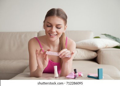 Young smiling woman filing her nails with emery board lying on couch at home, happy girl making manicure on leisure with lacquer bottles set other tools on sofa, hands care, time for yourself concept - Powered by Shutterstock