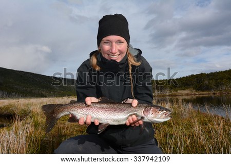 Young smiling woman fishing a big rainbow trout, Patagonia, Chile