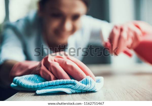 Young Smiling Woman in Gloves Cleaning House.\
Closeup of Happy Beautiful Girl wearing Protective Gloves Cleaning\
Desk by spraying Cleaning Products and wiping with Sponge. Woman\
Cleaning Apartment