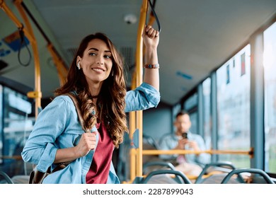 Young smiling woman holding onto a handle while traveling by public bus.