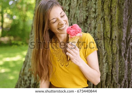 Young smiling woman with ice cream in countryside, tree in background